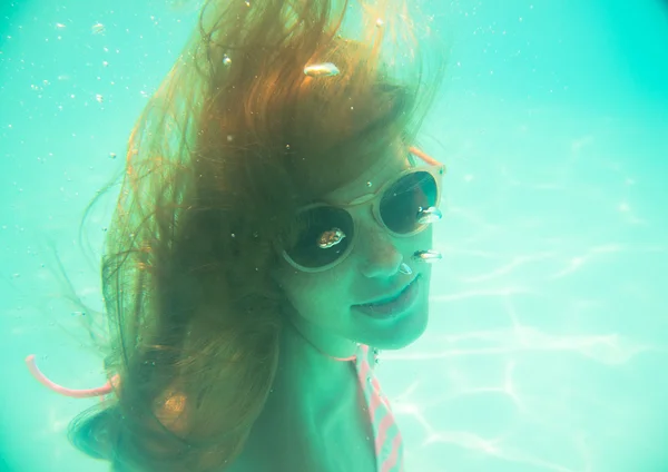 Young girl in sunglasses swimming underwater — Stock Photo, Image