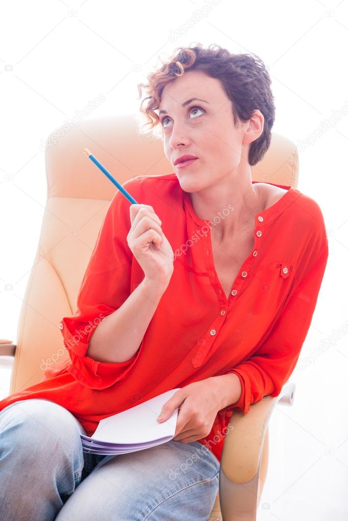 Girl sitting on a leather chair and holding a pencil and notepad