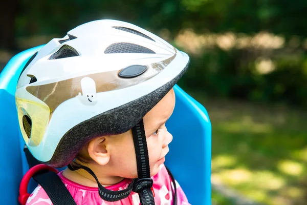 Bambina vestita con casco da bicicletta e si siede su un seggiolino per bicicletta — Foto Stock
