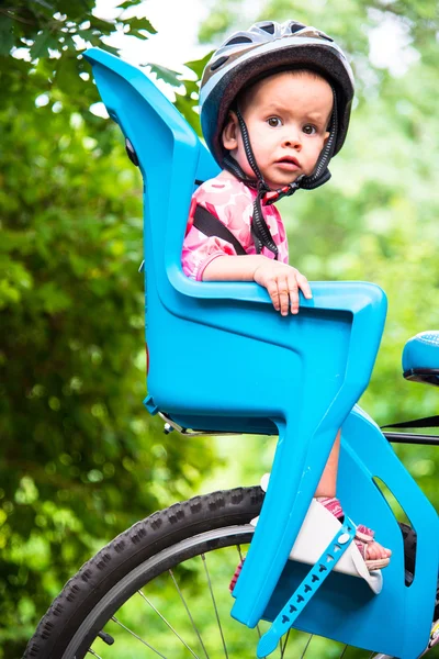 Μικρό κορίτσι ντυμένοι με κράνος ποδηλάτων και κάθεται σε ένα κάθισμα ποδηλάτου — Φωτογραφία Αρχείου