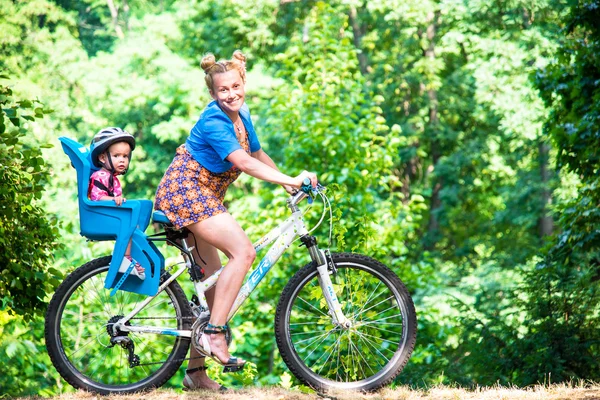 Mamá en una bicicleta con un niño pequeño, que llevaba un casco de bicicleta y — Foto de Stock