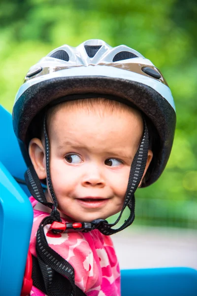Bambina vestita con casco da bicicletta e si siede su un seggiolino per bicicletta — Foto Stock
