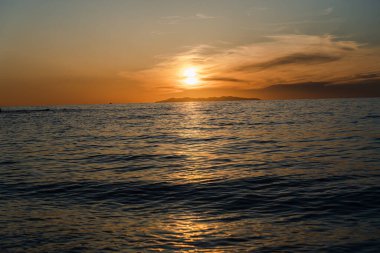 Ufuktaki uzak dağlarla denizin üzerinde altın gün batımı.