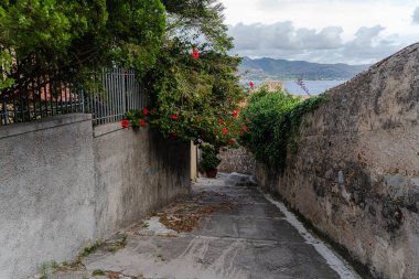 Taş duvarları, bitkileri, deniz ve dağları olan dar bir sokak..