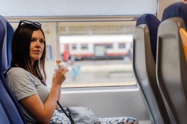 Trenin penceresinde oturan kadın seyahat sırasında sandviç yiyor..