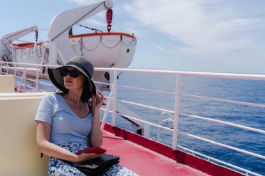 Feribot güvertesinde oturan kadın yolculuk sırasında denize bakıyor..