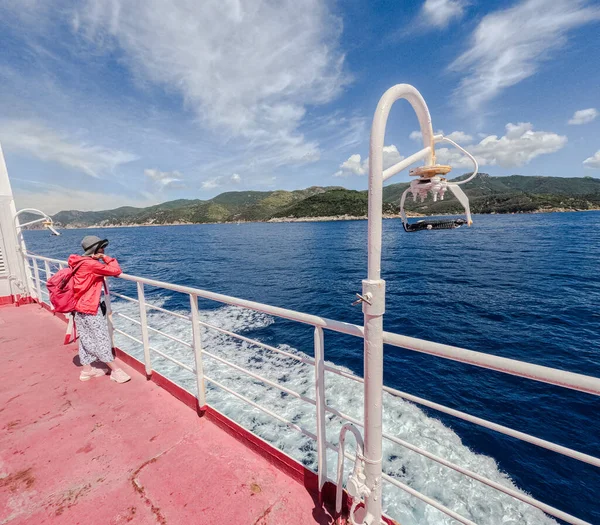 Feribot güvertesinde durup deniz ve kıyı şeridine bakan bir kadın..