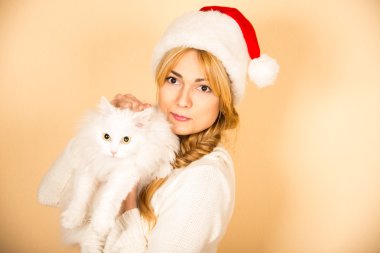 Kabarık beyaz kedi Noel Baba şapkalı kız tutar