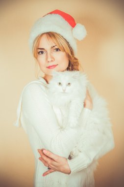 Kabarık beyaz kedi Noel Baba şapkalı kız tutar