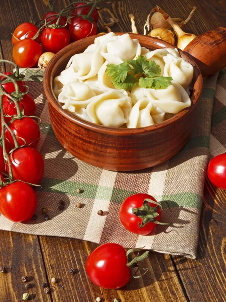 Dumplings with meat on a wooden table with tomatoes and onions — Stock Photo, Image