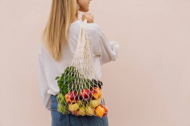 Alışveriş için tekrar kullanılabilir eko çanta. Elinde meyve dolu bir torba tutan genç bir kadın. Sıfır atık, plastiksiz konsept. Eko yaşam tarzı. Eko-alışveriş. Bilinçli tüketim. Çevre trendi. Boşluğu kopyala