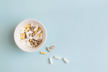 Haplar, kapsüller, vitaminler ve açık mavi arka planda beyaz tabakta doğal organik gıda takviyeleri. Minimum modern eczane ya da sağlık hizmeti konsepti. Düz konum, üst görünüm, kopyalama alanı