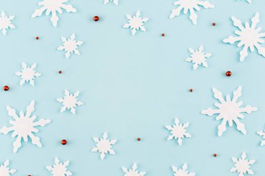 Noel kompozisyonu. Kar tanelerinden yapılmış desen, mavi arka planda kırmızı süslemeler. Noel, kış, yeni yıl konsepti. Asgari düzeyde. Düz yatış, üst görünüm. 