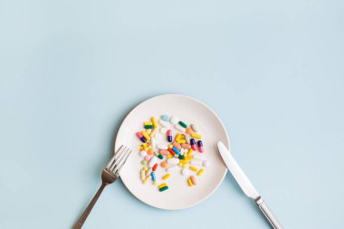 Renkli haplar, kapsüller ve açık mavi arka planda beyaz plaka üzerine takviyelerle yapılmış yaratıcı tıbbi düzen. Minimum modern eczane ya da sağlık hizmeti konsepti. Düz konum, üst görünüm, kopyalama alanı