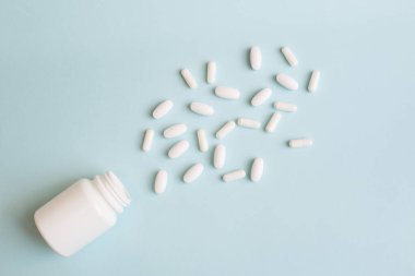 Beyaz haplar açık mavi arka planda beyaz şişeden döküldü. Asgari tıbbi konsept. Eczacılık, Covid-19 veya Coronavirus. Düz konum, üst görünüm, kopyalama alanı