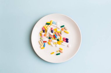Renkli haplar, kapsüller ve açık mavi arka planda beyaz plaka üzerine takviyelerle yapılmış yaratıcı tıbbi düzen. Minimum modern eczane ya da sağlık hizmeti konsepti. Düz konum, üst görünüm, kopyalama alanı