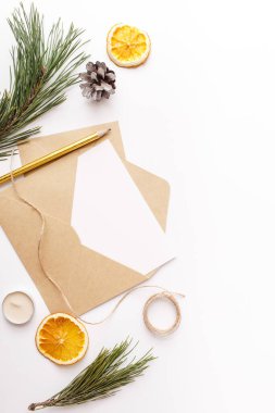 Noel, yeni yıl kompozisyonu. Kağıt boş maket, köknar ağacı dalları, kozalak, kurutulmuş portakal, tarçın çubukları, beyaz arka planda altın kalem mumları. Düz konum, üst görünüm, kopyalama alanı.