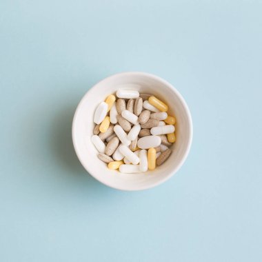 Haplar, kapsüller, vitaminler ve açık mavi arka planda beyaz tabakta doğal organik gıda takviyeleri. Minimum modern eczane ya da sağlık hizmeti konsepti. Düz konum, üst görünüm, kopyalama alanı