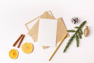 Noel boş tebrik kartı sahnesi. Kağıt boş, köknar ağacı dalları, kozalak, kurutulmuş portakal, tarçın çubukları, beyaz arka planda altın kalem mumları. Düz konum, üst görünüm, kopyalama alanı