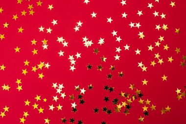 Kırmızı kağıtta yıldız şeklinde altın konfeti. Bayram arkaplanı. Doğum günün kutlu olsun, yeni yıl. Sevgililer Günü. Düz konum, üst görünüm, kopyalama alanı