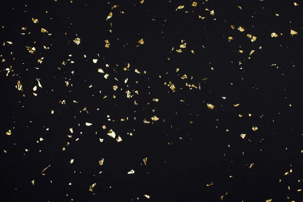 Gold confetti on black background. Festive holiday backdrop. Birthday congratulations Christmas New Year. Flat lay, top view, copy space