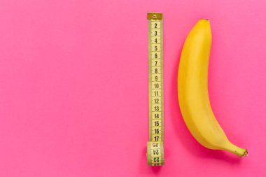 Yellow banana with measurement tape on pink background. Men penis size concept. Flat lay, top view, copy space