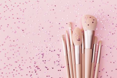 Makyaj fırçası ve parlak ışıltılı konfeti pastel pembe arka planda. Makyaj malzemeleri tatil konsepti. Düz konum, üst görünüm, kopyalama alanı.