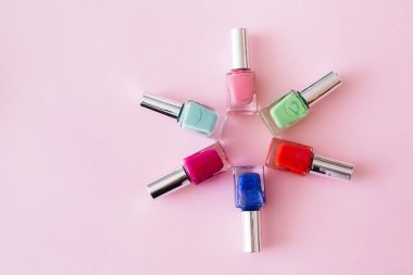 Pastel pembe arka planda renkli tırnak cilası şişeleri. Manikür ve pedikür konsepti. Düz konum, üst görünüm, kopyalama alanı.