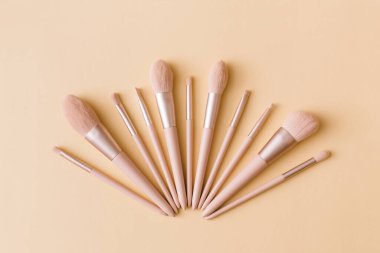 Bej arka planda makyaj fırçaları. Pastel renkte kadın güzellik aksesuarı. Düz konum, üst görünüm, kopyalama alanı.
