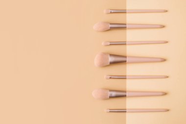 Bej arka planda makyaj fırçaları. Pastel renkte kadın güzellik aksesuarı. Düz konum, üst görünüm, kopyalama alanı