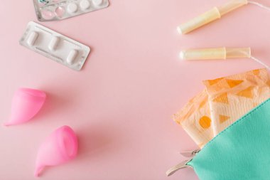 Kadınsal hijyen ve koruma ürünleri, hijyenik pedler, tamponlar, ağrı kesiciler ve pembe arka planda regl kupası. Üst görünüm, düz görünüm, kopyalama alanı.