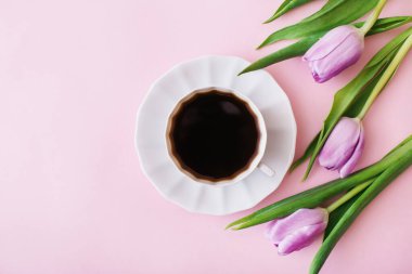 Pembe arka planda bir fincan kahve ve mor laleler. Düz konum, üst görünüm, metin için boşluk kopyala. Çiçek kompozisyonu. Bahar sabahı konsepti