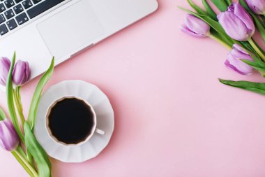 Bilgisayarlı çalışma alanı, lale çiçekleri, pembe arka planda bir fincan kahve. Merkez ofis masası. Düz konum, üst görünüm, metin için boşluk kopyala. Bahar konsepti