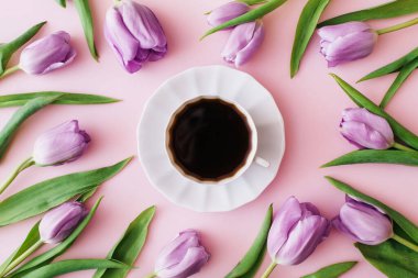 Pembe arka planda bir fincan kahve ve mor laleler. Düz yerde, üst tarafta. Çiçek kompozisyonu. Bahar sabahı konsepti