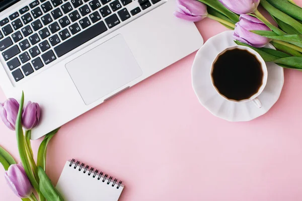 Espaço de trabalho com laptop, flores de tulipa, xícara de café em fundo rosa. Escritório de casa. Flat lay, vista superior, espaço de cópia para texto. Conceito Primavera. — Fotografia de Stock
