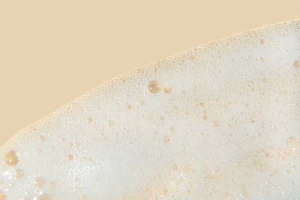 White cosmetics foam texture on beige background. Cleanser, shampoo bubbles, wash - liquid soap, shower gel, shampoo. Texture of white foam on rose background. Cosmetics banner with copy space