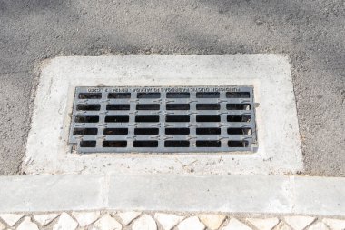 Close up of a metal storm drain grating embedded in a paved road, ensuring efficient water drainage and preventing flooding