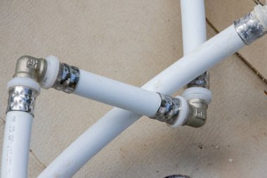 Two white plastic pipes connected by metal fittings lie on a piece of cardboard, ready for a plumbing project