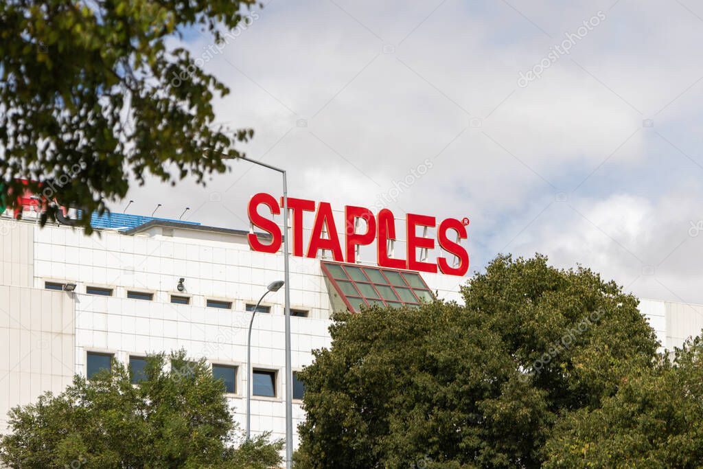 Staples retail store building displays prominent red logo sign against a cloudy sky, representing office supplies, electronics, and printing services