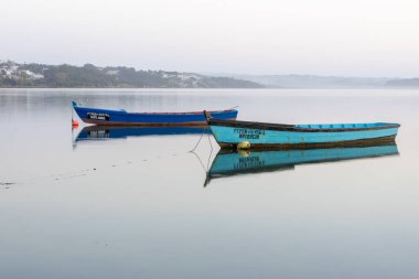 Two traditional fishing boats drifting on still water with an early morning mist