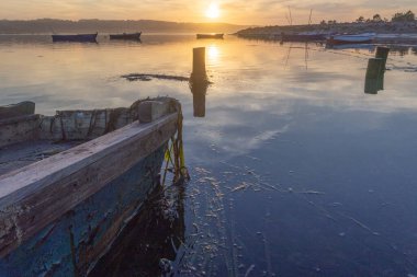 Tranquil water reflecting golden sunset light over an old fishing boat