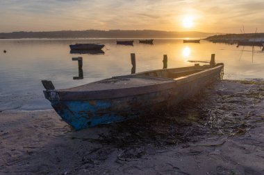 Sakin bir gündoğumu sırasında kumlu bir sahilde dinlenen eski bir tekne.
