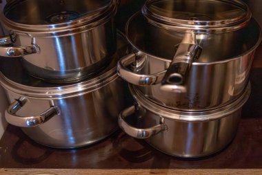 Mutfak rafına konmuş paslanmaz çelik tencere ve tavalar.