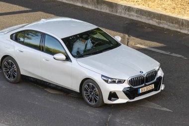 Asfalt yolda giden beyaz BMW sedan, bir sürücüyü gideceği yere götürüyor.