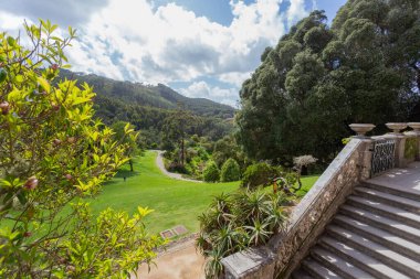 Bereketli yeşillik, tarihi merdivenler ve bulutlu bir gökyüzünün altındaki bahçe mimarisinin yer aldığı Monserrate Parkı