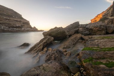 Gün batımında kayaların ve kayalıkların etrafında akan uzun pozlu su