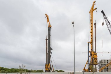 Sanayi kazma platformları bulutlu gökyüzünün altındaki kentsel inşaat sahasında sondaj yapıyor.
