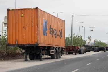 Turuncu hapag Lloyd konteynırı yolun kenarındaki park halindeki bir kamyon römorkunda.