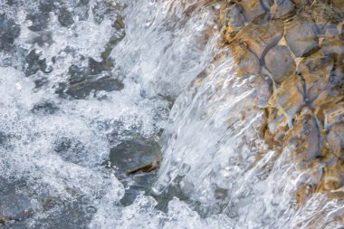 Akan su, su sıçrıyor ve pürüzsüz nehir kayaları üzerinde kabarcıklar oluşturuyor.