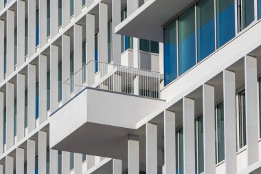 Beyaz geometrik cepheli modern mimari ve mavi gökyüzü yansımasına karşı asılmış balkon.